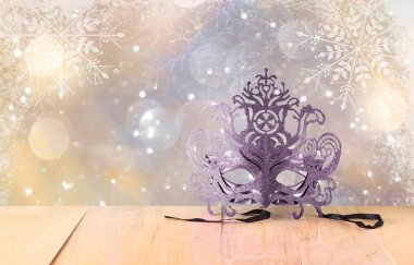 Kar tanesi bindirmeleri ahşap masa ve glitter zemin üzerine gizemli Venedik maskeli balo maskesi