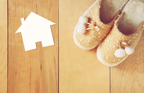 Vista superior de las zapatillas de mujer cálidas sobre el piso de madera y la forma de la casa de papel como concepto de bienvenida a casa —  Fotos de Stock