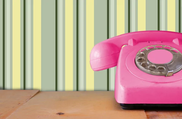 Retro pastelowy różowy telefon na drewnianym stole i streszczenie retro wzór geometryczny pastelowe tło. retro filtrowanego obrazu — Zdjęcie stockowe