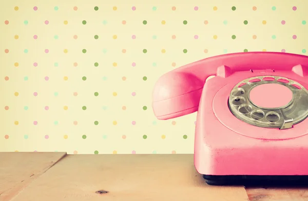 Retro pastellrosa Telefon auf Holztisch und abstrakt retro geometrischem Pastellmuster Hintergrund. Retro gefiltertes Bild — Stockfoto