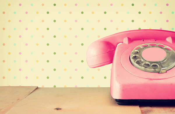 Retro pastel pink telephone on wooden table and abstract retro geometric pastel pattern Background. retro filtered image