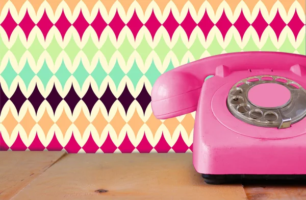 Retro pastellrosa Telefon auf Holztisch und abstrakt retro geometrischem Pastellmuster Hintergrund. Retro gefiltertes Bild — Stockfoto