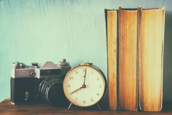 Stack of books, old clock and vintage camera over wooden table. image is processed with retro faded style — Stock Photo, Image