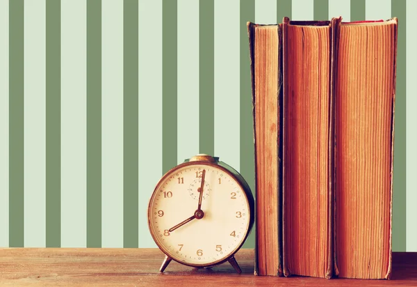 Stapel alter Bücher und alter Uhr über Holztisch und Vintage-Tapete — Stockfoto