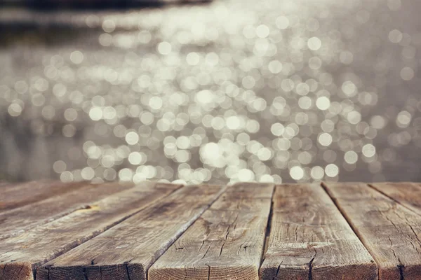 Holzbretttisch vor der sommerlichen Landschaft mit glitzerndem Seewasser. Hintergrund verschwommen — Stockfoto