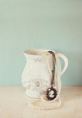 İnci ve romantik vintage takı koleksiyonu ile ahşap masa üzerinde beyaz klasik Victoria vazo. Retro filtre uygulanan görüntü. metin için yer