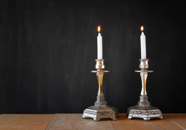 Dois castiçais com velas acesas sobre mesa de madeira e fundo de quadro-negro — Fotografia de Stock