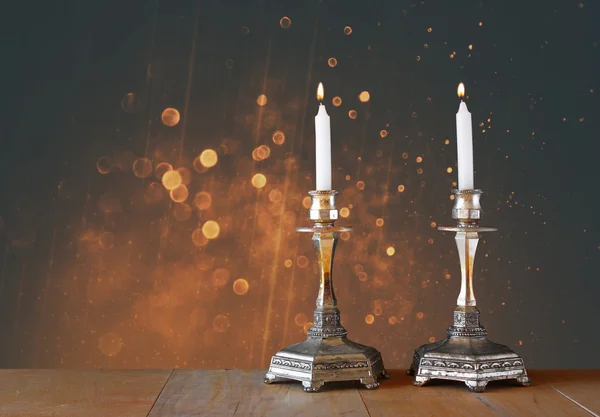 불타는 나무 테이블과 빈티지 반짝이 배경 위에 초와 두 촛대 — 스톡 사진
