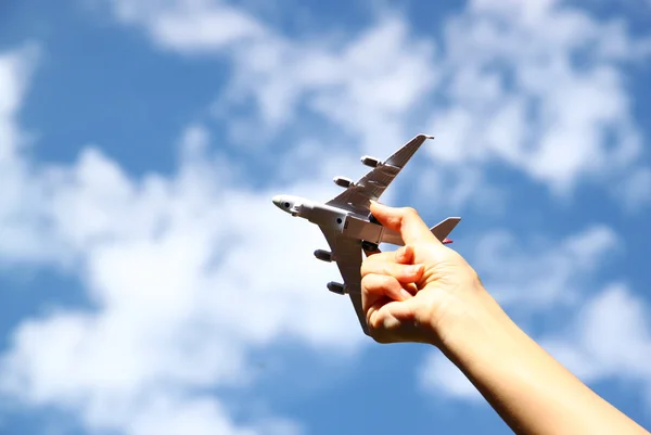 Κοντινό πλάνο φωτογραφία της γυναίκας χέρι κρατώντας παιχνίδι αεροπλάνο κατά μπλε ουρανό με σύννεφα — Φωτογραφία Αρχείου