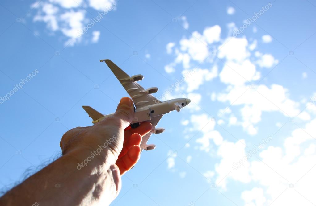 Close up photo of man's hand holding toy airplane against blue sky with clouds