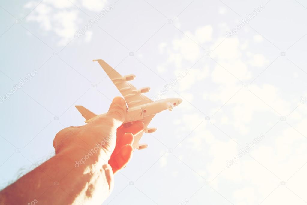 Close up photo of man's hand holding toy airplane against blue sky with clouds