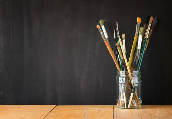 Paint brushes in jar over blackboard background