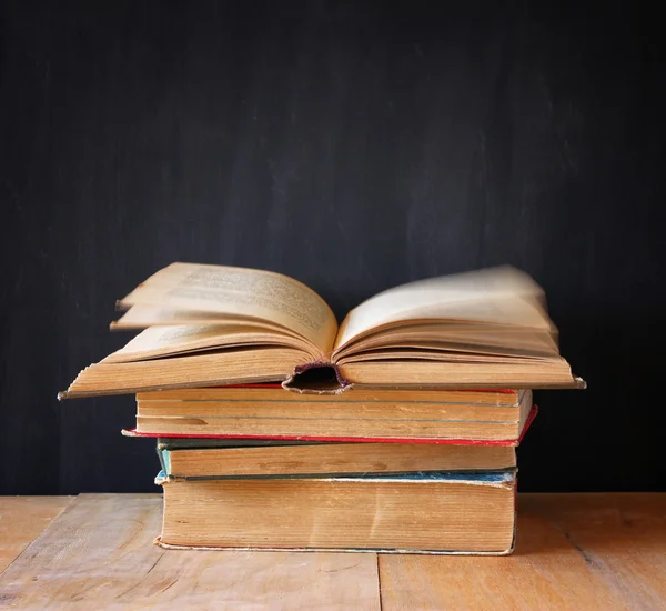 Stapel alter Bücher, oberes Buch offen und Seiten in Bewegung, über Holztisch und Holzuntergrund — Stockfoto