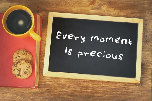 Top view of blackboard with the phrase every moment is precious next to coffee cup over wooden table — Stock Photo, Image