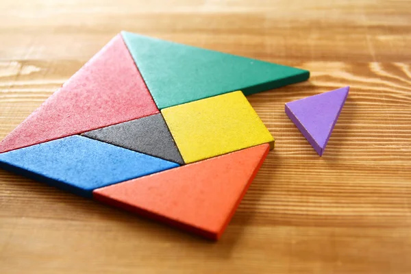 Chybějící kousek do čtvercové tangram puzzle, dřevěný stůl. — Stock fotografie