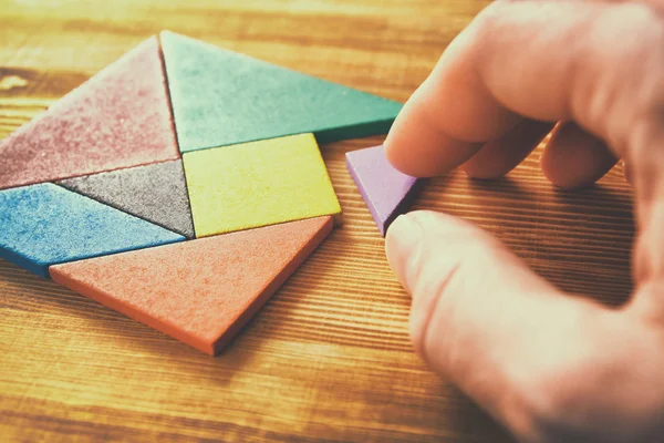 Chybějící kousek do čtvercové tangram puzzle, dřevěný stůl. — Stock fotografie