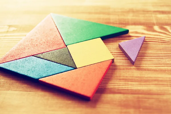 Chybějící kousek do čtvercové tangram puzzle, dřevěný stůl. — Stock fotografie