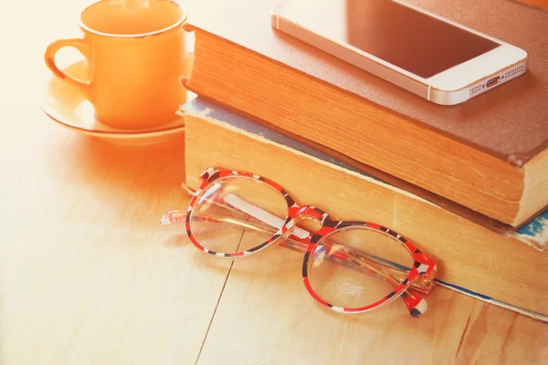 Reading glasses, stack of  old books and smartphone over wooden table, retro filtered image — Stock Photo, Image