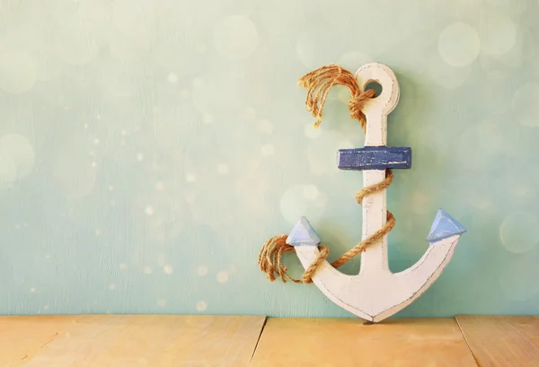 Old nautical anchor on wooden table over wooden aqua background and glitter overlay — Stock Photo, Image