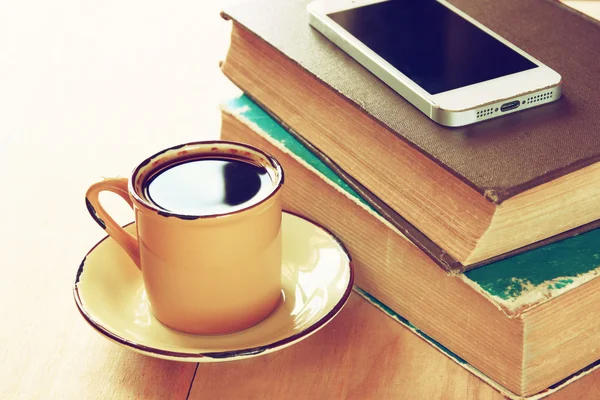 Cup of coffee, stack of old books and smartphone over wooden table, retro filtered image — Stock Photo, Image