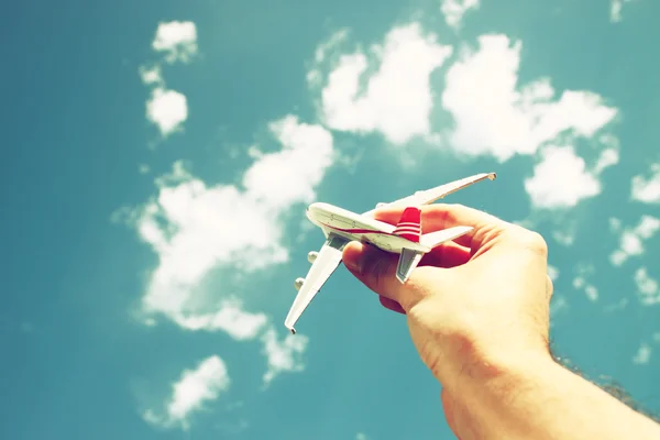 Foto de perto da mão do homem segurando avião de brinquedo contra o céu azul com nuvens. imagem filtrada — Fotografia de Stock