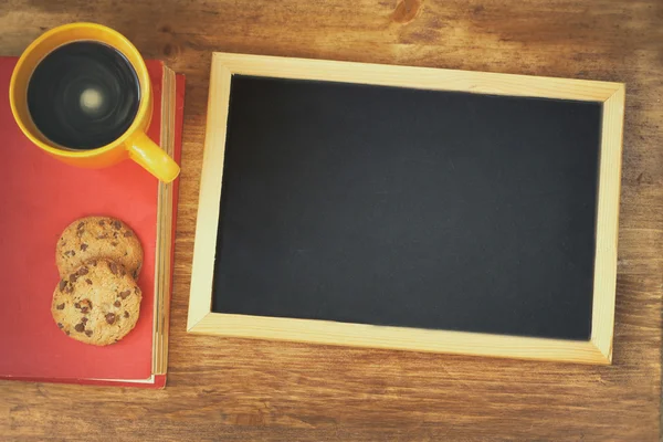 木製のテーブルの上のコーヒー カップの横にある空の黒板の上から見る — ストック写真