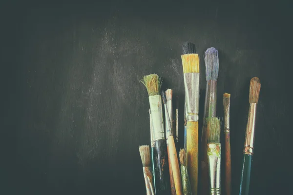 Paint brushes in jar over blackboard background — Stock Photo, Image