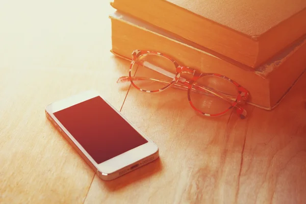 Leesbrillen, stapel van oude boeken en slimme telefoon over houten tafel, retro gefilterde afbeelding — Stockfoto