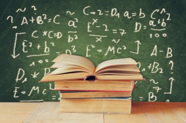 Image of school books on wooden desk over green background with formulas. education concept