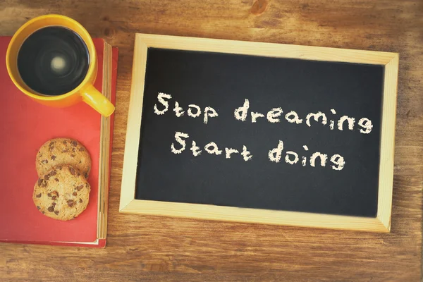 Top view image of blackboard with the phrase stop dreaming start doing, next to coffee cup and cookies — Stock Photo, Image