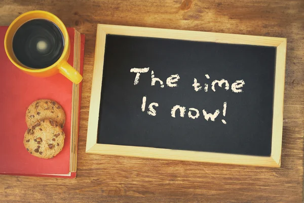 Quadro negro com a frase o tempo agora está escrito nele, ao lado de xícara de café e biscoitos — Fotografia de Stock
