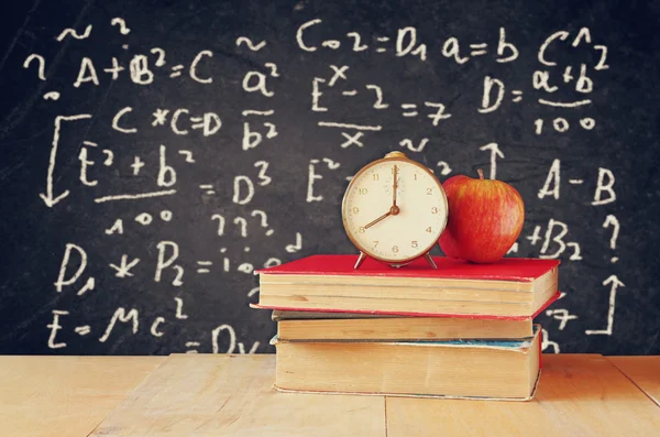Imagen de libros escolares sobre escritorio de madera, manzana y reloj vintage sobre fondo negro con fórmulas. concepto de educación —  Fotos de Stock