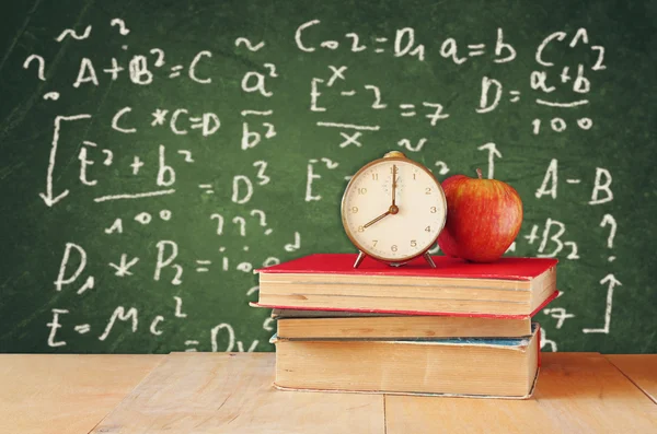 Imagen de libros escolares sobre escritorio de madera, manzana y reloj vintage sobre fondo verde con fórmulas. concepto de educación — Foto de Stock