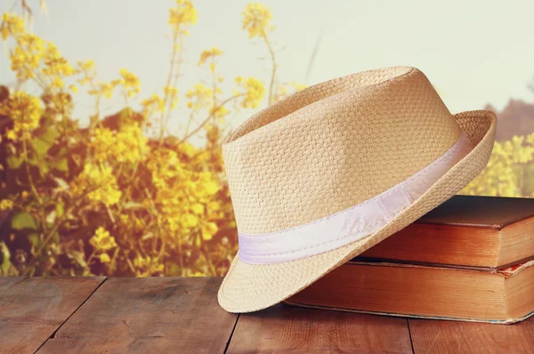 Sombrero Fedora y pila de libros sobre mesa de madera y fondo de la naturaleza floral del país. concepto de relajación o vacaciones — Foto de Stock