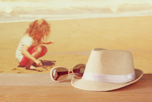 Fedora Hut und Sonnenbrille über Holztisch und Meereslandschaft Hintergrund. Entspannung oder Urlaubskonzept — Stockfoto