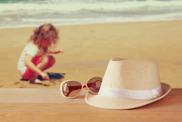 Fedora kalap és napszemüveg, fából készült asztal és tengeri táj háttér. relaxáció vagy a pihenés fogalmát — Stock Fotó