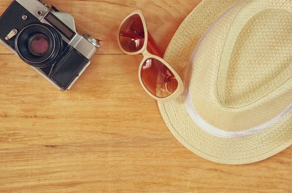 Κάτοψη του κομψό καπέλο γυναίκα παλιά φωτογραφική μηχανή γυαλιών ηλίου πάνω από το ξύλινο τραπέζι. έννοια vaction και ταξίδια — Φωτογραφία Αρχείου