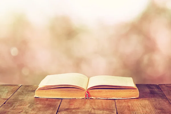 Libro abierto sobre mesa rústica de madera frente a borrosas luces bokeh — Foto de Stock