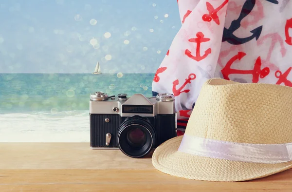 Fedora hat, old vintage camera and scarf over wooden table and sea landscape background. relaxation or vacation concept — Stock Photo, Image