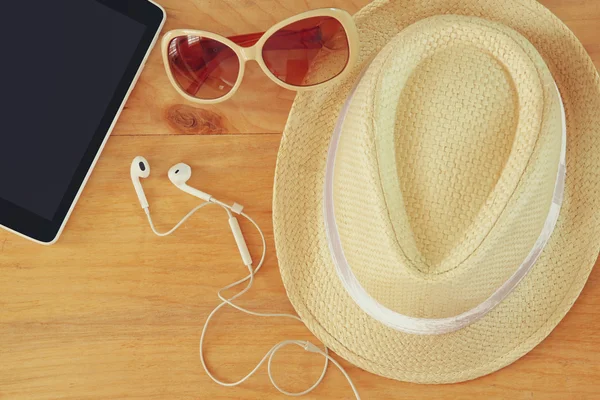 Bovenaanzicht van stijlvolle hoed vrouw zonnebril en tablet apparaat over houten tafel. vakantie en reizen concept — Stockfoto