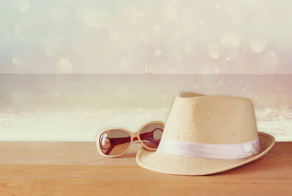 Fedora Hut und Sonnenbrille über Holztisch und Glitzerhintergrund. Entspannung oder Urlaubskonzept — Stockfoto