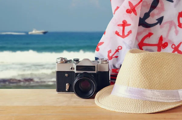 Fedora kalap, régi vintage kamera és sálat, fából készült asztal és tengeri táj háttér. relaxáció vagy a pihenés fogalmát — Stock Fotó