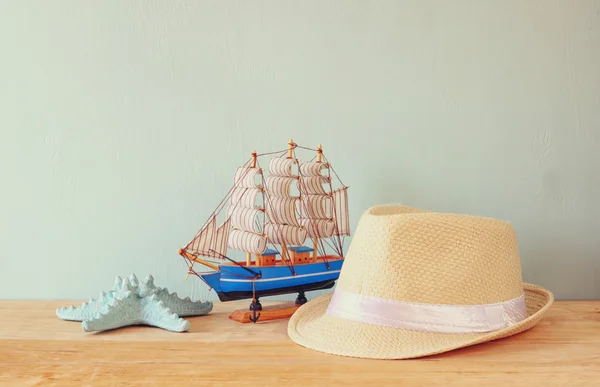 Fedora hat, wooden boat and starfish over wooden table and blue background. relaxation or vacation concept — Stock Photo, Image