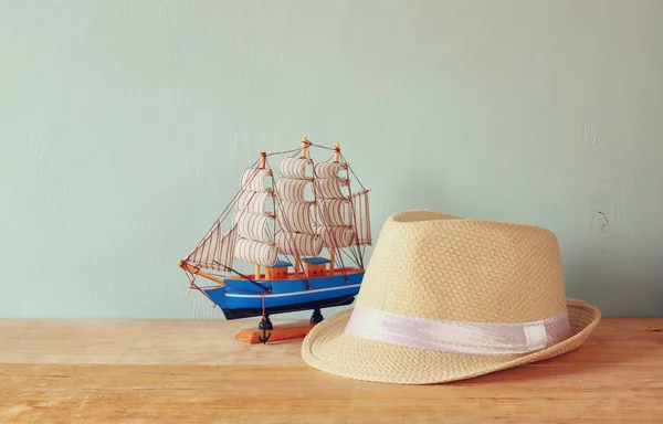 Fedora Hut und Holzboot über Holztisch und blauem Hintergrund. Entspannung oder Urlaubskonzept — Stockfoto