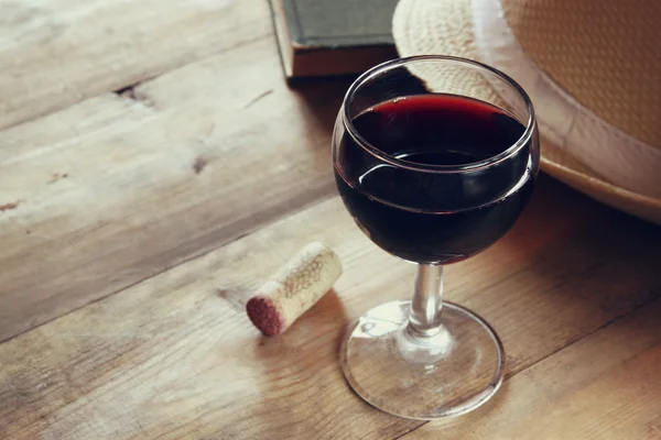 Red wine glass and old book on wooden table at sunset burst. vintage filtered image — Stock Photo, Image