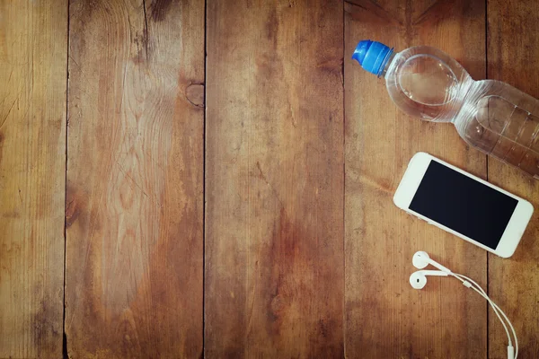 Fitness concept met fles water, mobiele telefoon met koptelefoon op houten achtergrond. gefilterde afbeelding — Stockfoto