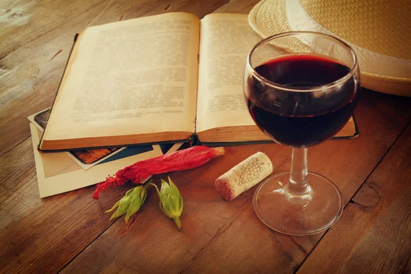 Sklenice na červené víno a staré otevřená kniha na dřevěný stůl v západu slunce praskla. Vintage filtrovaného obrazu — Stock fotografie