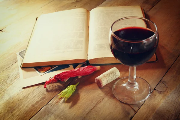 Copa de vino tinto y viejo libro abierto sobre mesa de madera al atardecer estalló. vintage imagen filtrada —  Fotos de Stock