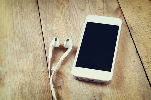 Vue du dessus du téléphone intelligent blanc et des écouteurs sur la table en bois — Photo