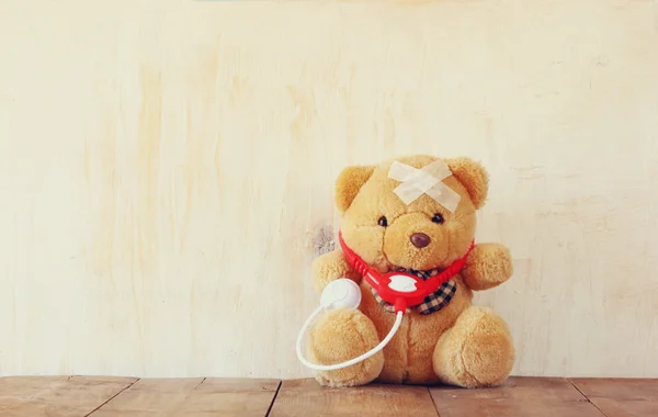 Urso de pelúcia com bandagem e estetoscópio sobre fundo de madeira — Fotografia de Stock